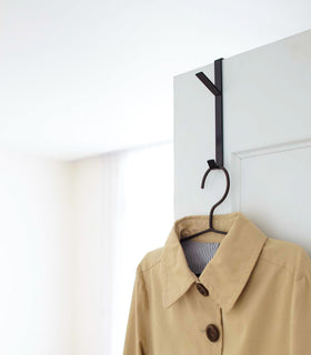 Black Over-the-Door Hanger displaying jacket on closet door by Yamazaki Home. view 5