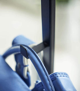 Close up view of black Rolling Coat Rack hook holding blue backpack by Yamazaki Home. view 11