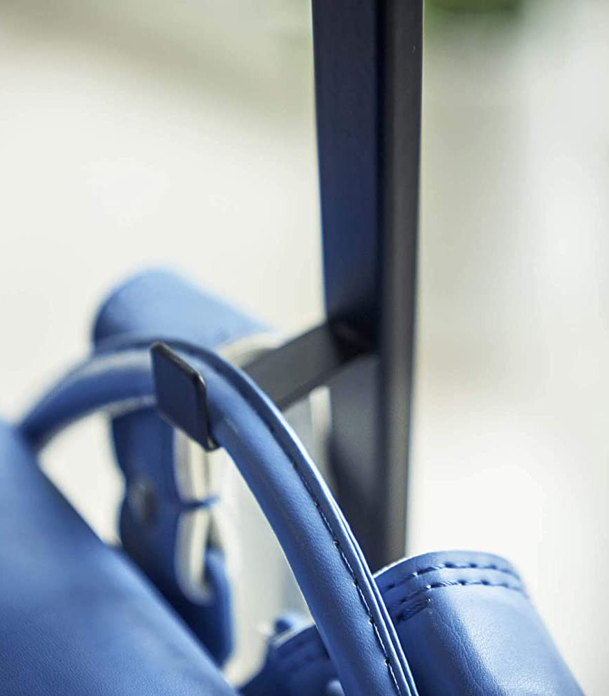 View 11 - Close up view of black Rolling Coat Rack hook holding blue backpack by Yamazaki Home.