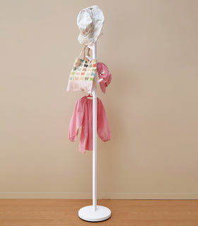 White coat rack in the shape of a tree hung with children's clothes and hats. view 4