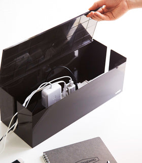 Aerial view of black Cable Managment Box holding wires and chargers on white background by Yamazaki Home. view 10
