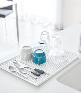 White Dish Drainer Tray holding silverware and cups on sink counter by Yamazaki Home. view 2