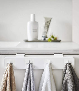 Front view of white Push Dish Towel Holder holding hand towels on bathroom sink cabinet by Yamazaki Home. view 6