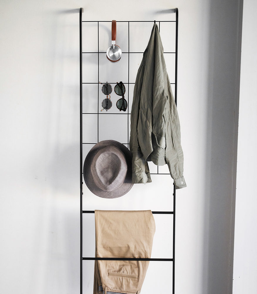 View 11 - Front view of black Leaning Ladder with Grid Panel displaying clothing and accessories by Yamazaki Home.