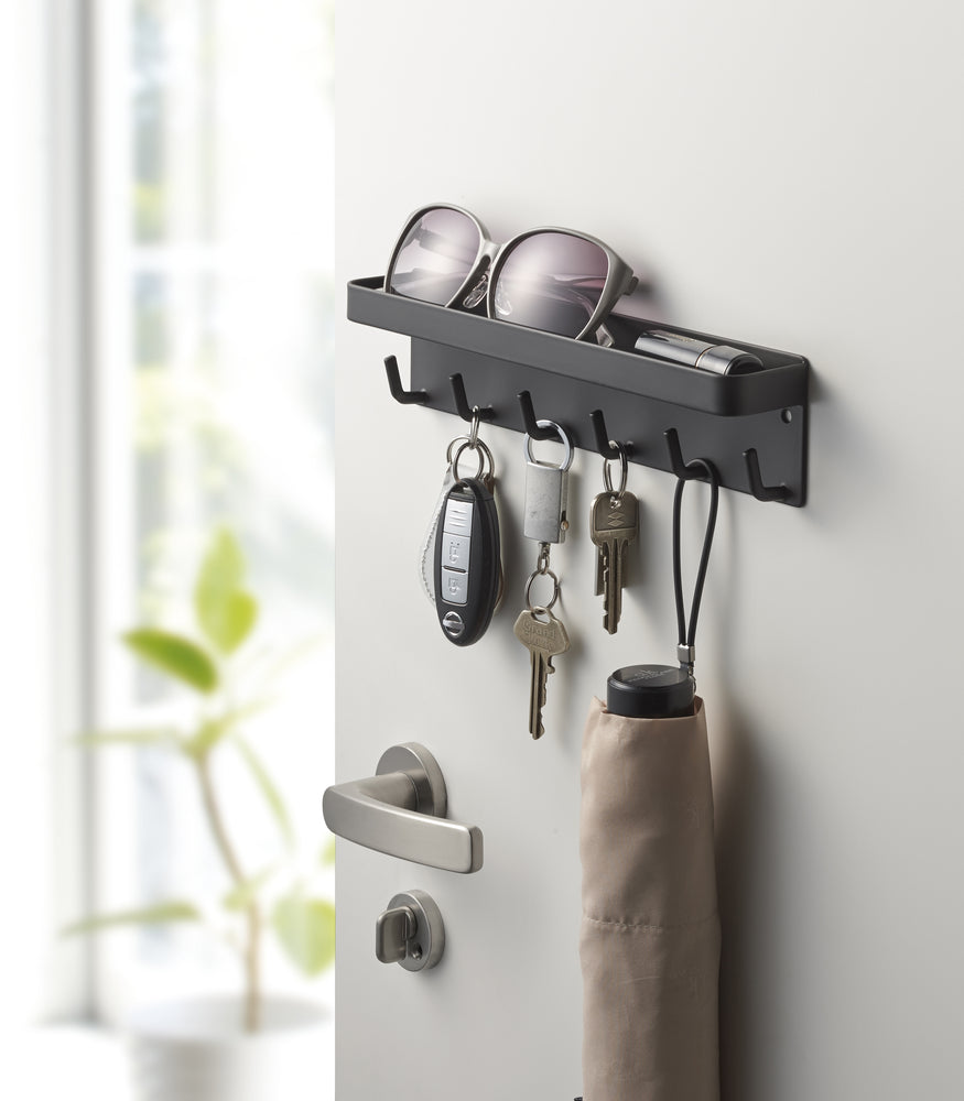 View 8 - Black Magnetic Key Rack with Tray holding keys, umbrella and sunglasses on door by Yamazaki Home.