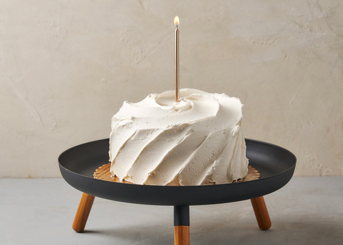 Birthday cake with one gold candle on a modern black cake tray from Yamazaki Home.