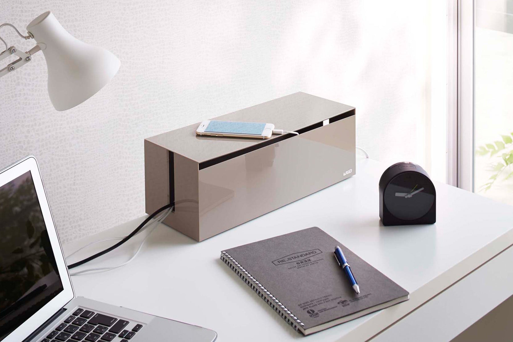 Cable Organization Box from Yamazaki Home on a modern desk next to a laptop, planner, desk light, and modern clock.