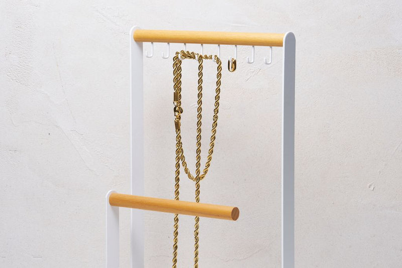 White Jewelry and Accessory Organizer from Yamazaki Home with hooks holding a gold chain necklace. 
