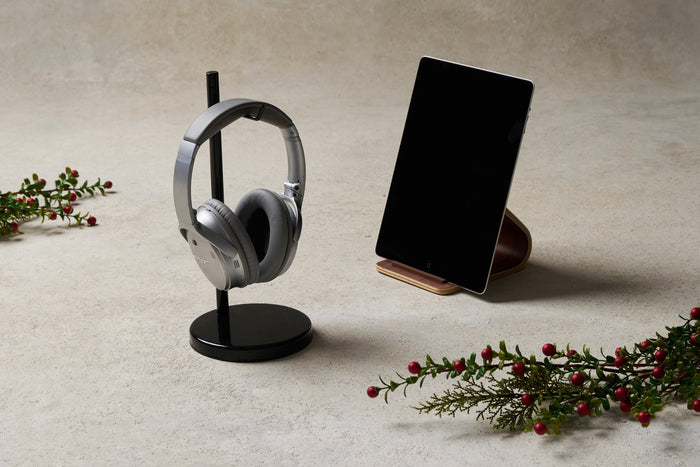 Elevated headphone stand in black holding Bose noise cancelling headphones. Molded wood tablet stand holding iPad. Setup decorated by garland. Featured image for the Tech Gift Guide 2025, Yamazaki Home.