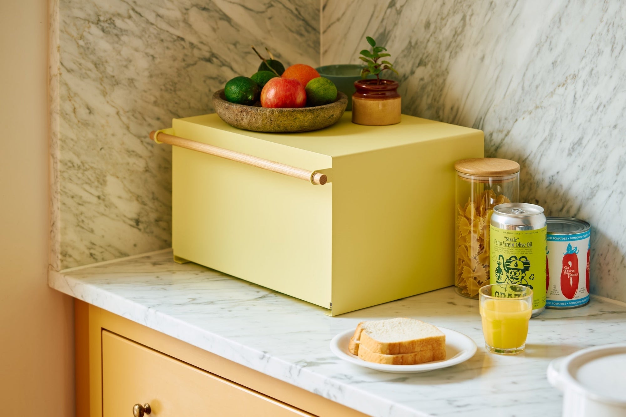 Yellow bread box from yamazaki home in a cozy yellow kitchen with fruit and various pantry items. 