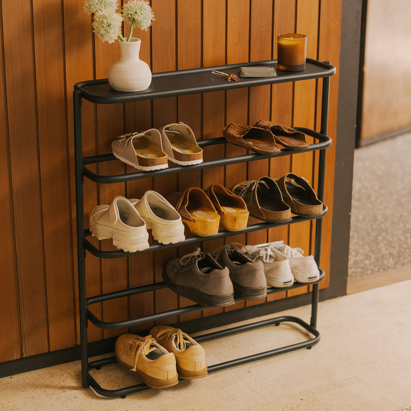 Black metal 4-tier shoe rack organizer for entryways, styled with flowers and candle against wood wall