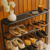 Black metal entryway shoe rack with flat top shelf holding flowers, candle, and keys, filled with sandals and clogs