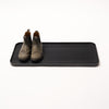 Black steel boot tray with ridged bottom holding a pair of boots with a white backdrop. Designed by Apto. 