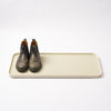 Ivory steel boot tray with ridged bottom holding a pair of boots with a white backdrop. Designed by Apto.