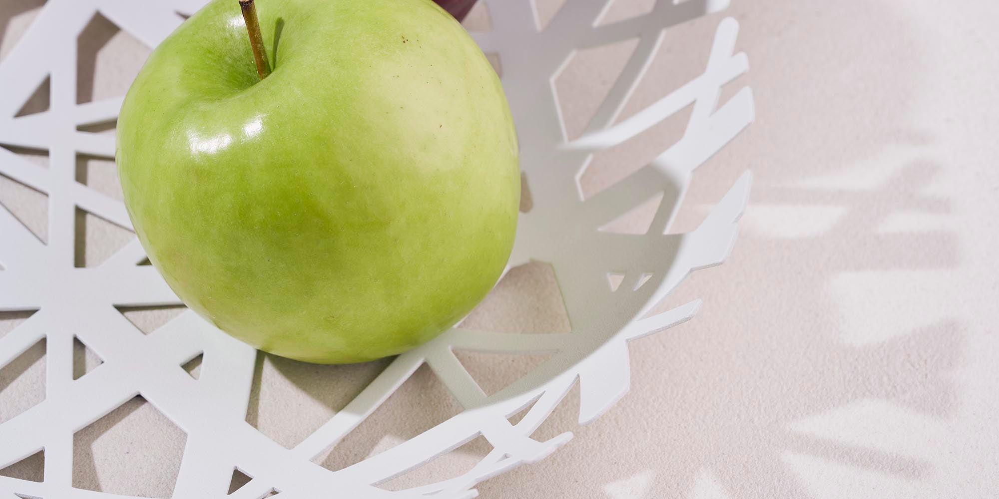 Yamazaki Home Fruit Bowl in white steel holding a large green apple. Close up image for collection cover photo.