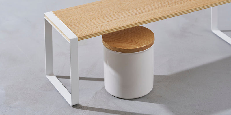 Single-Tier Riser with white steel risers and wood tabletop. White ceramic jar with wood top underneath the riser. 