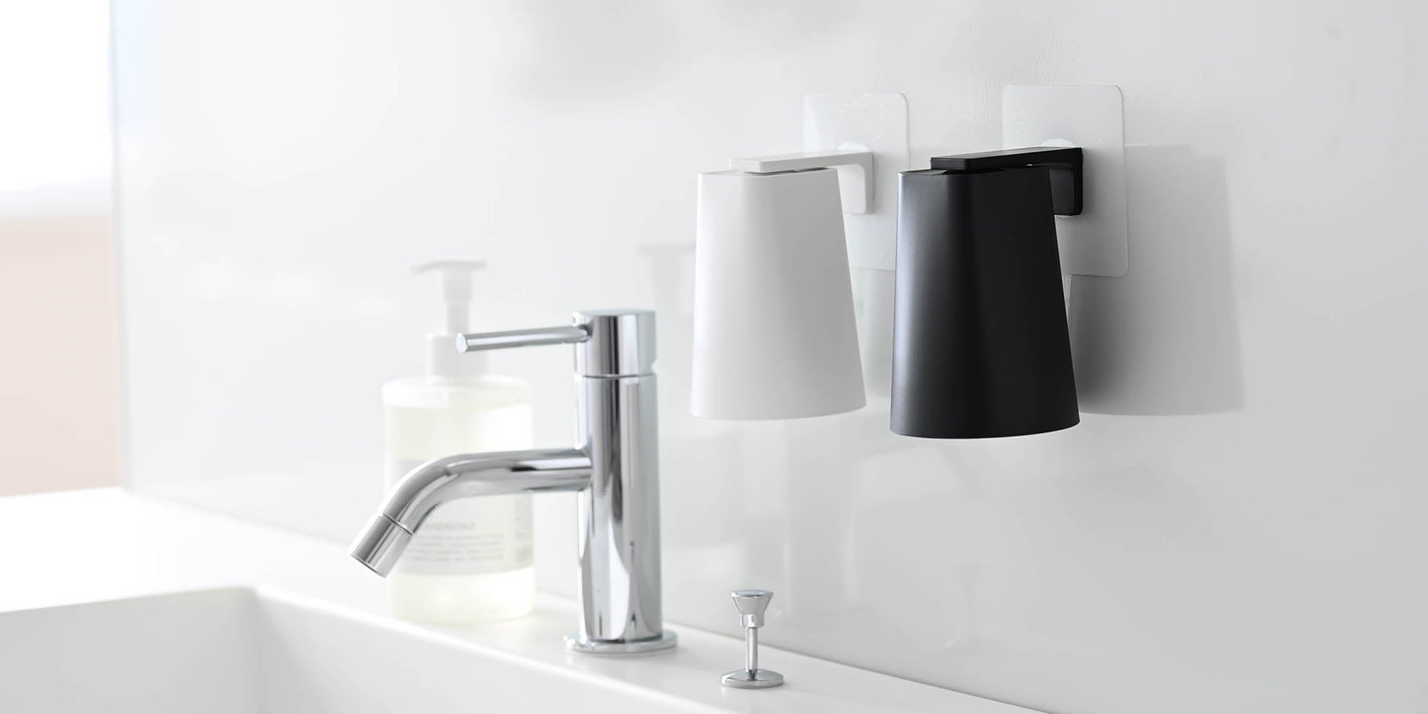 Two Traceless Adhesive Magnetic Cups mounted above the bathroom sink. One white cup and one black cup. 