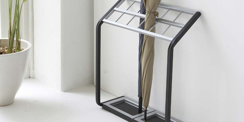 Black and steel Umbrella Stand from Yamazaki Home holding a tan umbrella and gray umbrella in a modern entryway. 