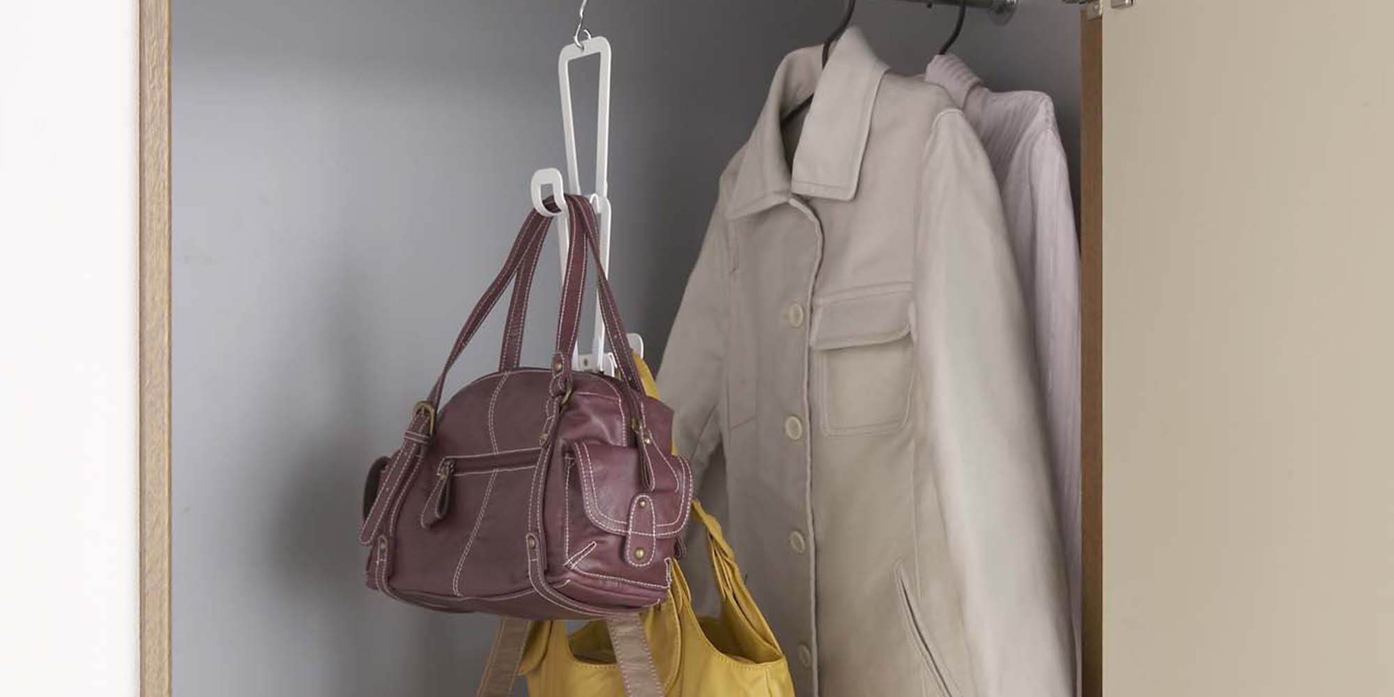 Cascading storage hooks in white from Yamazaki Home holding various purses hanging in a closet. 