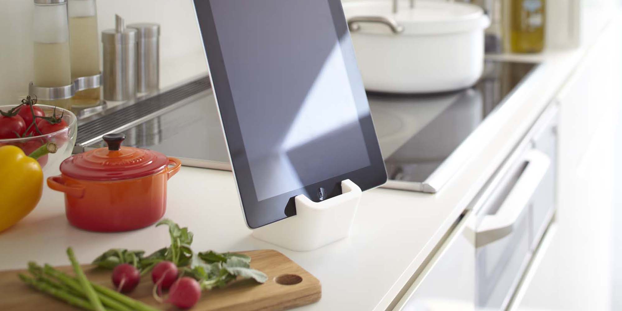 Yamazaki Home Square tablet stand holding a black iPad in a modern kitchen. The counter also has cutting board with beets, bell peppers and a bright orange Le Creuset Mini Round Cocotte (pot).