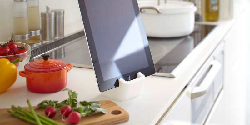 Yamazaki Home Square tablet stand holding a black iPad in a modern kitchen. The counter also has cutting board with beets, bell peppers and a bright orange Le Creuset Mini Round Cocotte (pot).