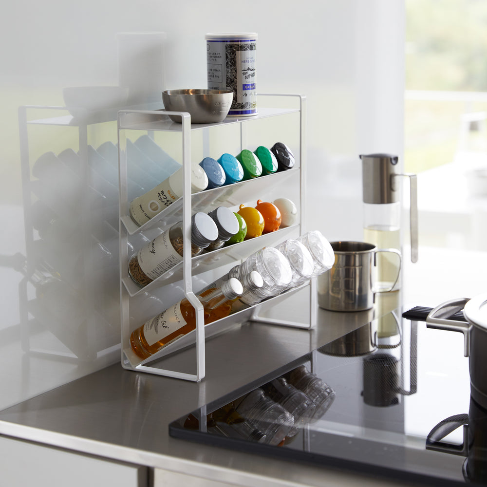 View 13 - White Four-Tier Slim Spice Rack by Yamazaki Home on a sleek kitchen counter, filled with colorful spices and kitchen essentials.