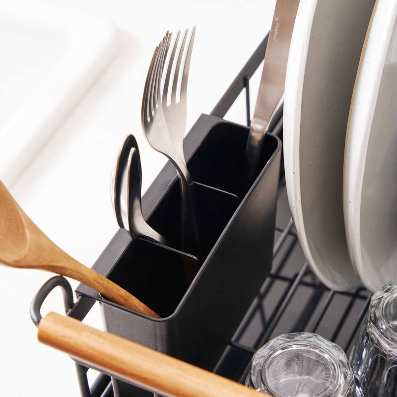 Removable utensil holder holding three forks on a black dish drying rack with wood handles in a modern kitchen.