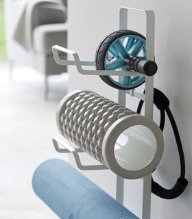 Close up view of Yamazaki Home White Fitness Equipment Storage Rack holding a yoga mat and foam rollers. view 6