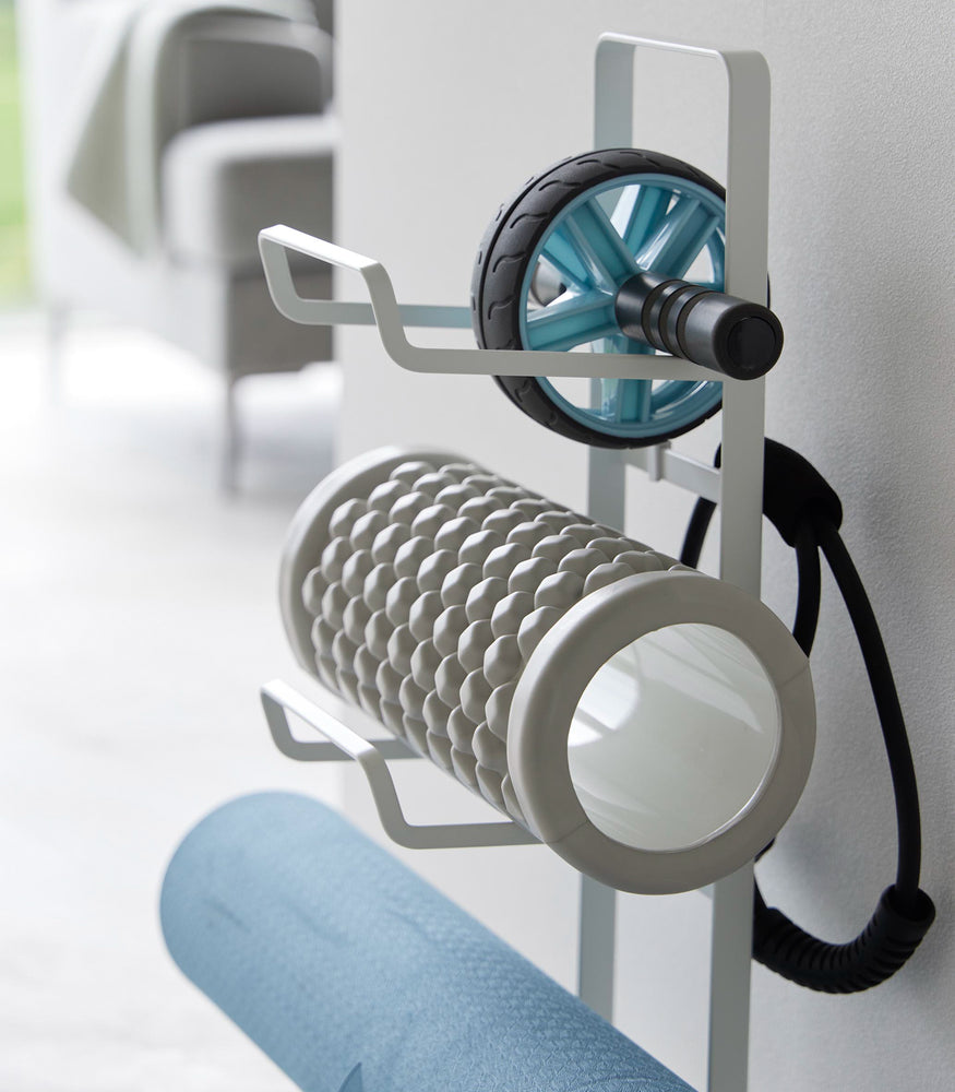 View 6 - Close up view of Yamazaki Home White Fitness Equipment Storage Rack holding a yoga mat and foam rollers.