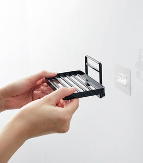 Hands installing Yamazaki Home's black Traceless Adhesive Soap Tray on a bathroom wall, demonstrating its ease of use. view 14