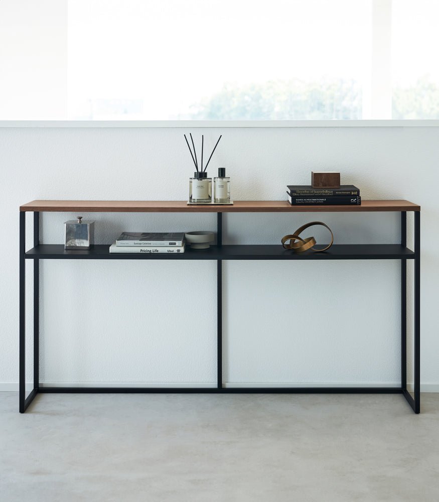View 32 - Frontal image of black Yamazaki Home Long Console Table - Shelf against a wall with books and decorations on it
