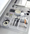 Close-up image of four different sizes of stackable clear organizers—small, medium, large, and deep—neatly placed in a bathroom drawer. Made from transparent material, they accommodate items like brushes and sanitary products, showcasing their clarity and stackability.