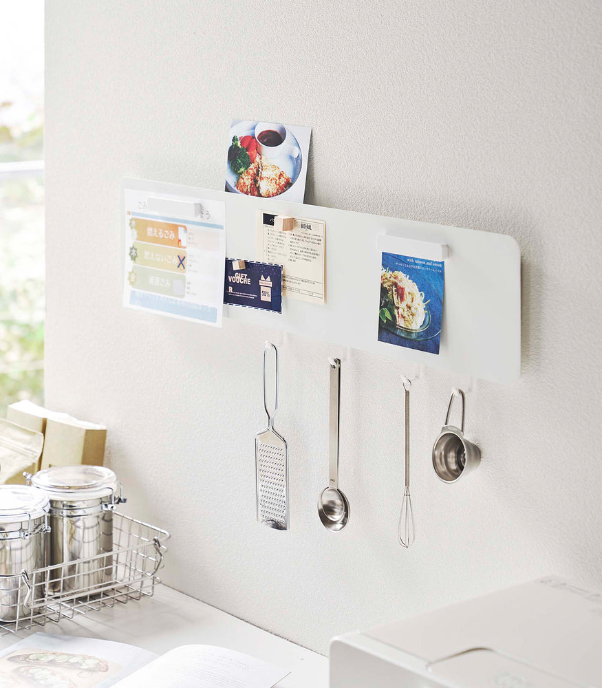 View 1 - Magnetic Wall Panel in white by Yamazaki Home on a wall with various recipes tacked on and kitchen utensils hanging from bottom hooks.