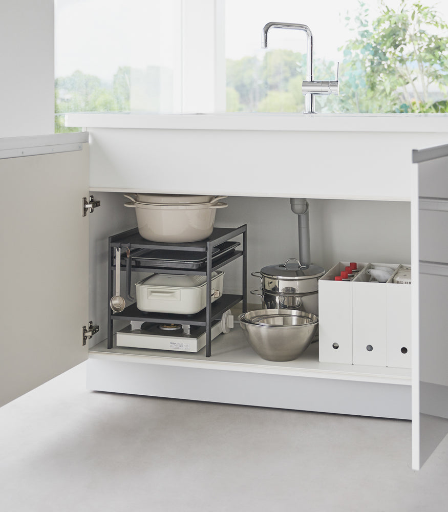 View 10 - Yamazaki Home Black Three-Tier Cabinet Storage Rack is holding a pot and pans under the kitchen sink.