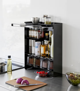 Diagonal view of the Concealable Spice Rack in black by Yamazaki Home with the front panel open, showing various spices and condiments inside. view 11
