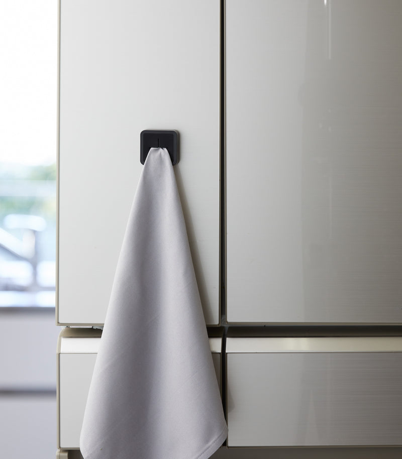 Frontal view of black Yamazaki Home Traceless Adhesive Towel Holder with towel inserted