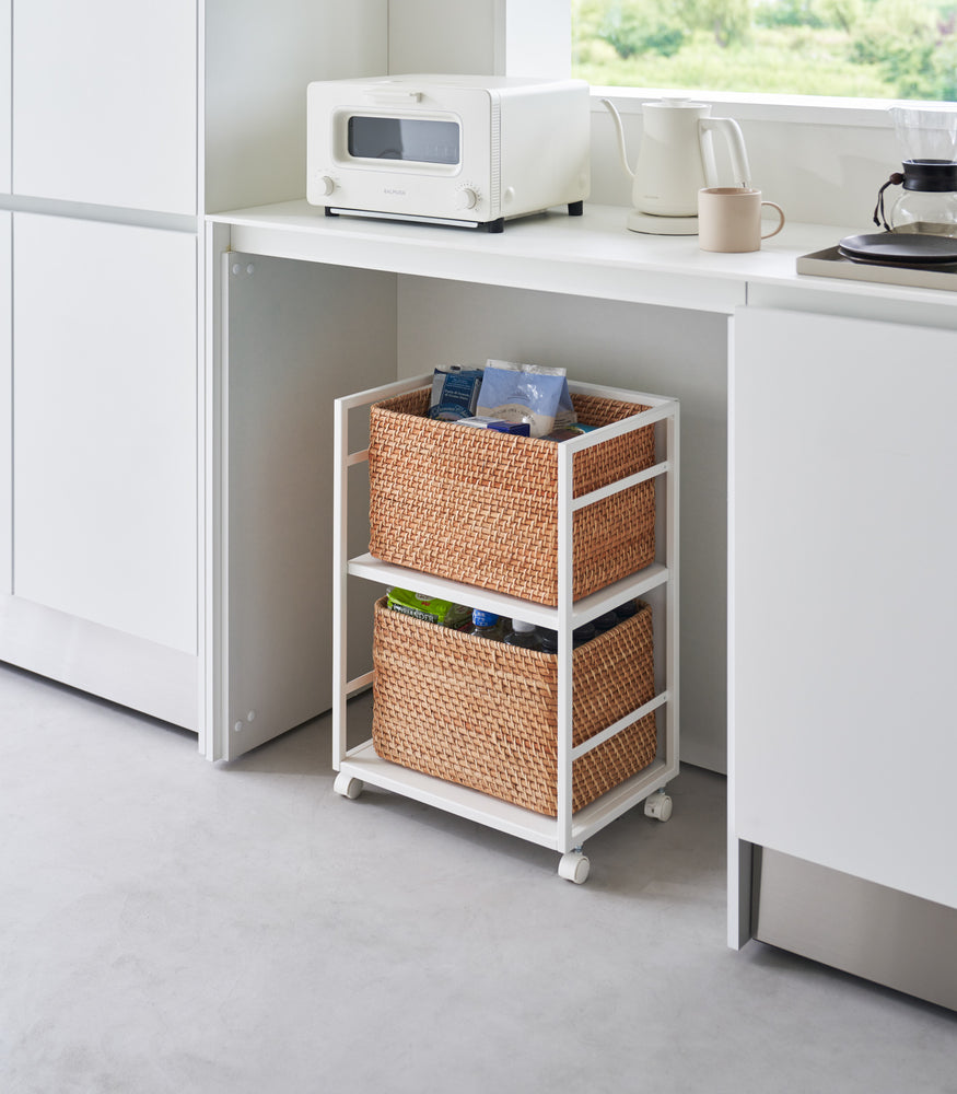 View 2 - Two-level white steel storage cart with casters is shown in an opening of a recessed cabinet. Cart houses storage bins on both levels. One side of the cart has a wall to hide storage.