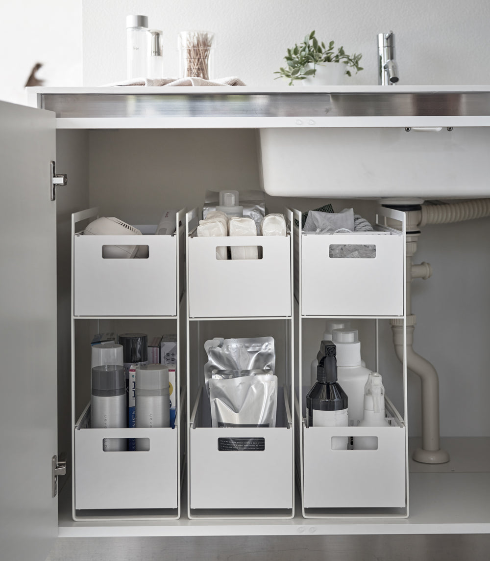 Three two-tier storage bins are displayed in an under-a-sink cabinet. Both levels of each hold various cleaning products and supplies.