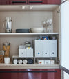 Front view of white Yamazaki Home Shelf Risers in a cabinet containing water bottles and wrap boxes