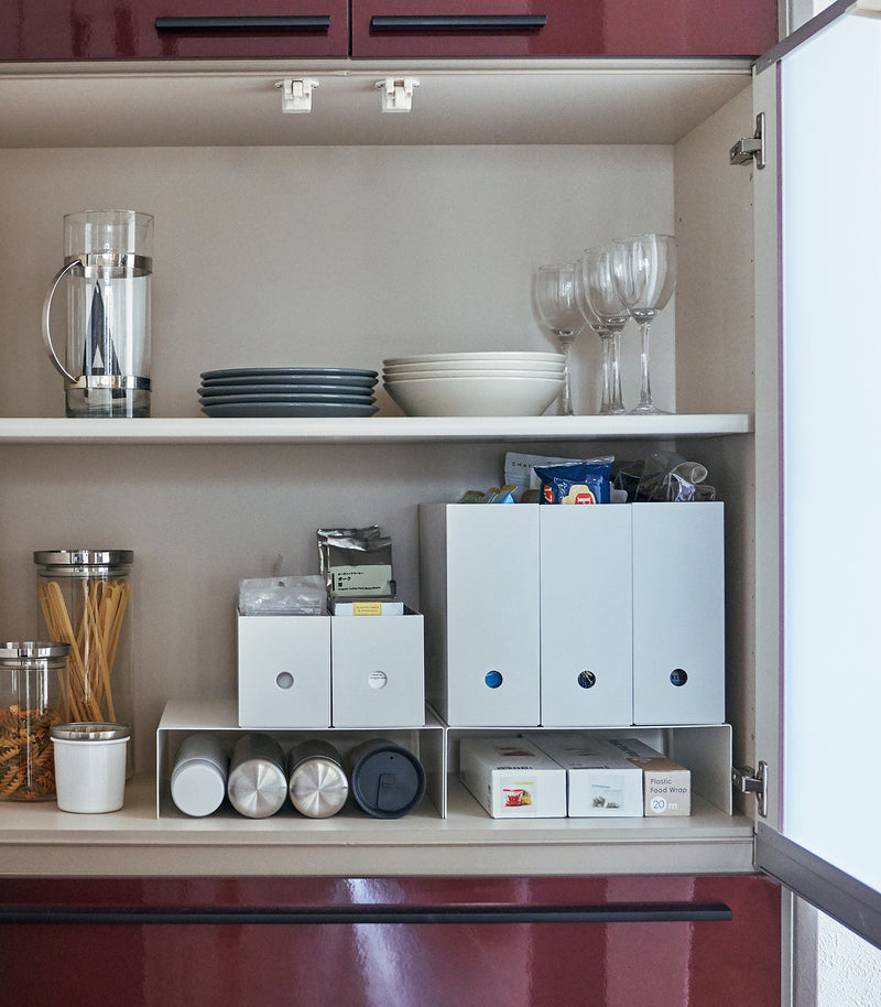 Front view of white Yamazaki Home Shelf Risers in a cabinet containing water bottles and wrap boxes