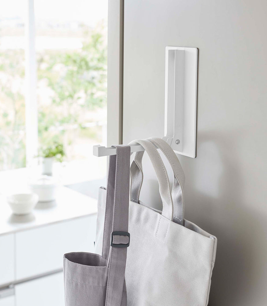 View 6 - Close up of white Yamazaki Home Magnet Folding Hanger open with multiple tote bags hung