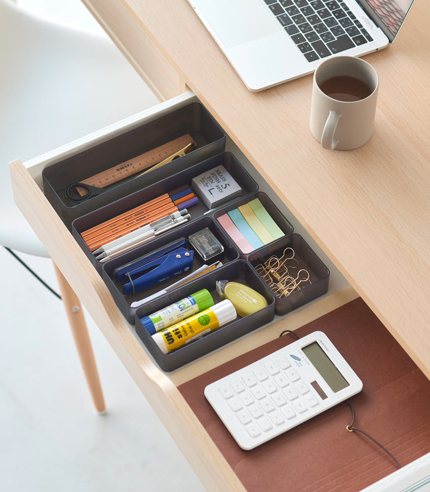 View 59 - Three different sizes of stackable clear organizers in black—small, medium, and large—are neatly placed in a desk drawer. Made from transparent material, they accommodate stationery items like pens, paper clips, and sticky notes, showcasing their clarity and stackability.