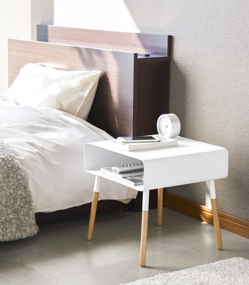 View 3 - White Short Storage Table holding phone, book, and clock in bedroom by Yamazaki Home.