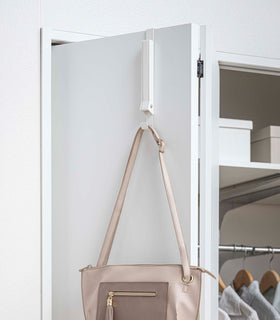 White Yamazaki Home Folding Over-The-Door Hanger closed with a single purse hung view 16