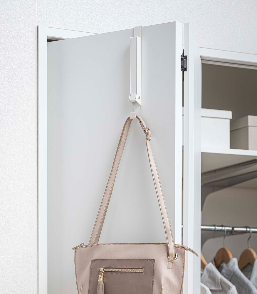 View 16 - White Yamazaki Home Folding Over-The-Door Hanger closed with a single purse hung