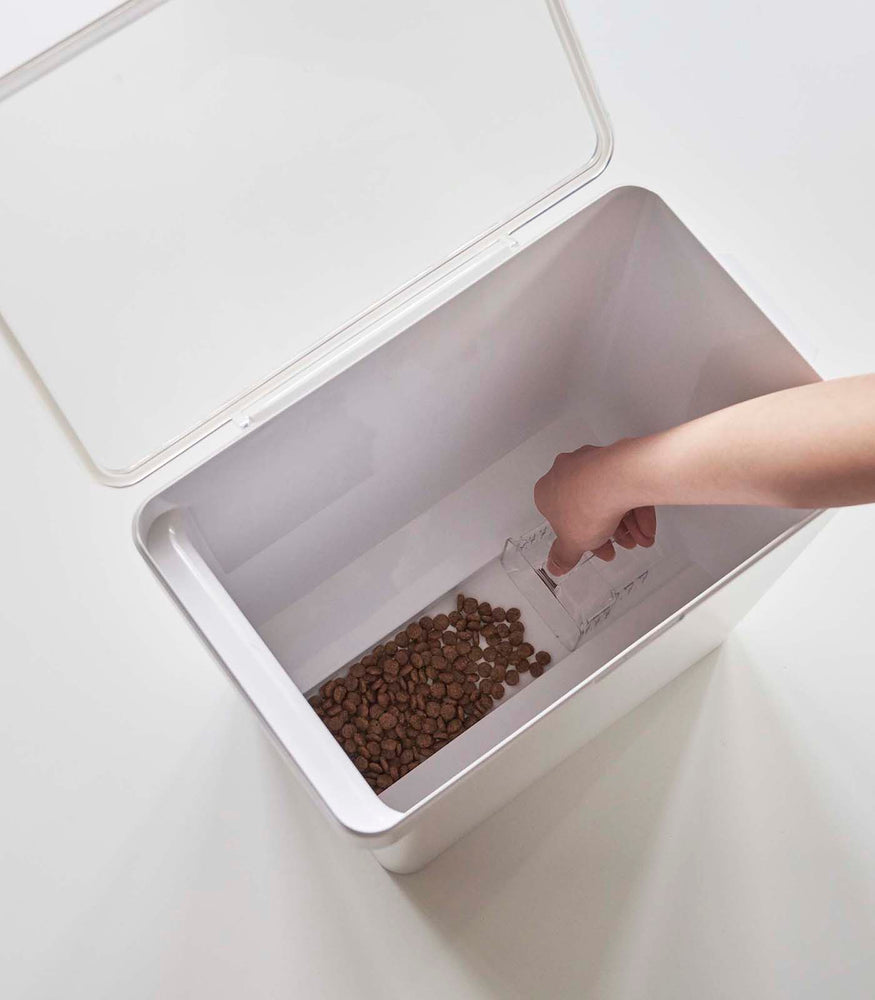 View 45 - Aerial view of person scooping pet food out of white Airtight Food Storage Container on white background by Yamazaki Home.