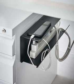 Close-up of Magnetic Under-Desk Cable Organizer in white by Yamazaki Home mounted on the side of a file cabinet holding a power strip and phone. view 16