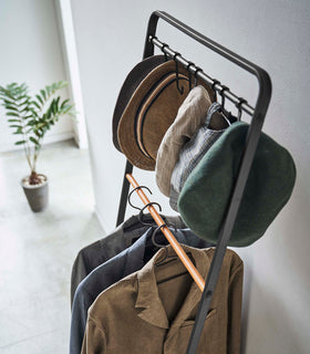 Top-down view of hats and clothes hung on black Yamazaki Home Coat Rack with Hat Storage view 16