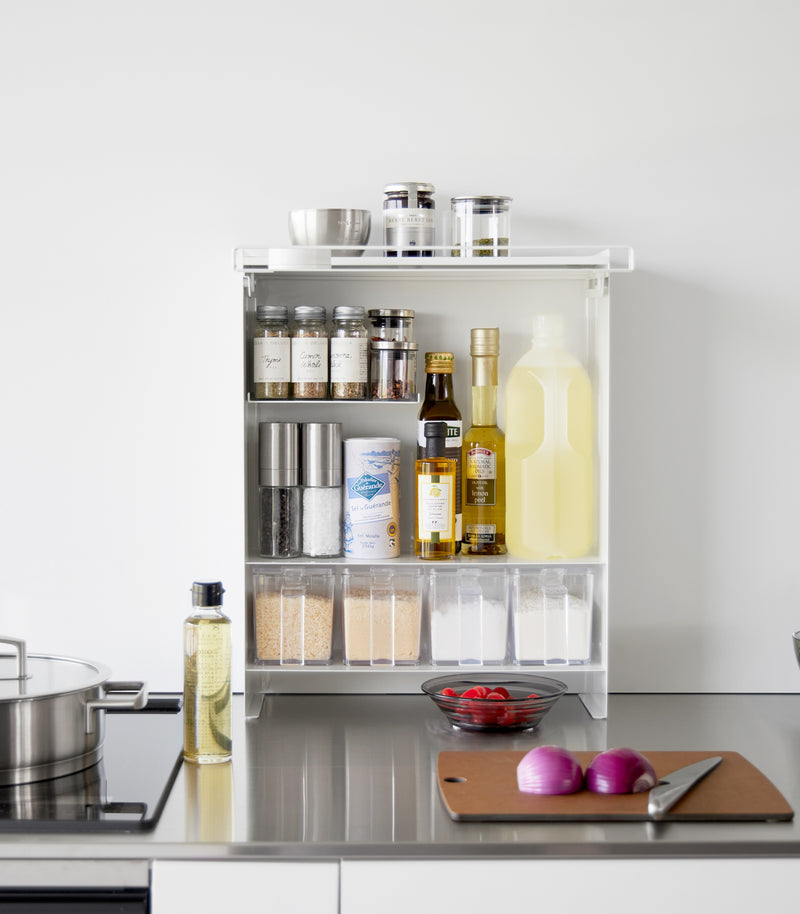 Front view of the Concealable Spice Rack in white by Yamazaki Home with the front panel open, showing various spices and condiments inside.