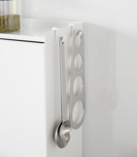 A close-up image of kitchen utensils hanging from hooks placed along the top ridge of the Concealable Spice Rack by Yamazaki Home in white. view 8
